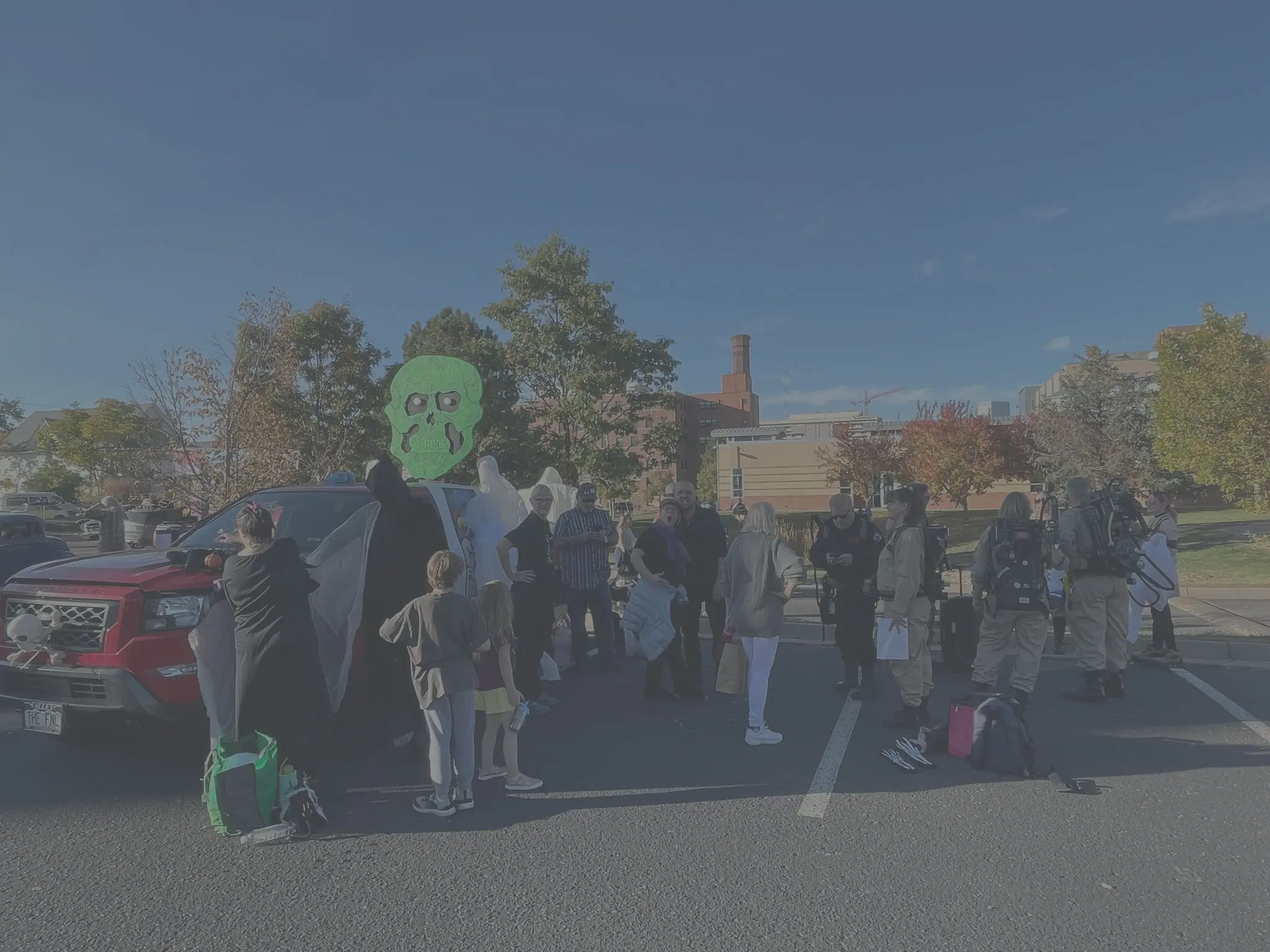 A group of people outside by a red truck loaded up with ghosts, people stand around facing the camera, others are Colorado Ghostbusters in proton packs getting ready to walk in a halloween parade