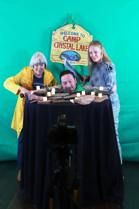 A cute blonde guy, Smurf, in blue jeans, a blue Ghostbuster shirt on, smiling while interviewing a beautiful blonde scream queen in a light blue top and pasiley pants in front of a small projector screen