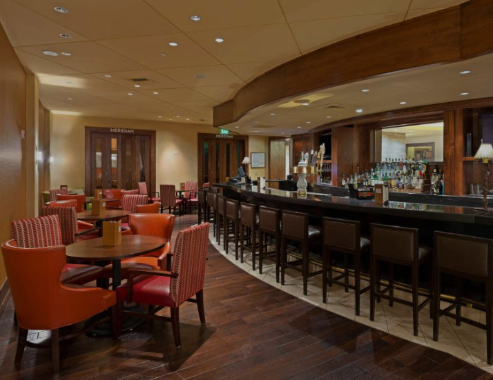 Bar inside hotel with red tables on the side and brown high top chairs at the bar