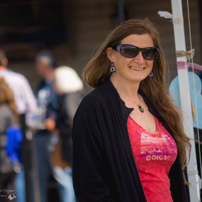 Becky, asmiling redhead in sunglasses, a black jacket and redish pink low cut colorado tshirt outside